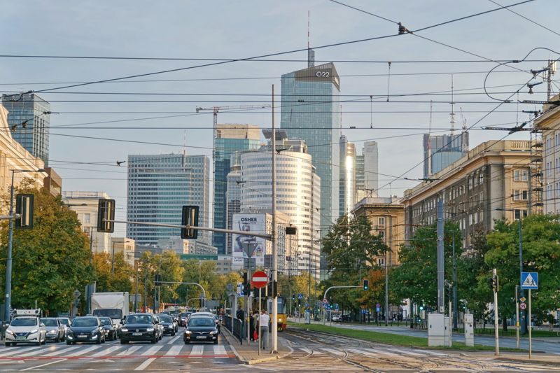 A busy urban intersection in the Wola district of Warsaw, Poland, featuring modern skyscrapers like the Q22
